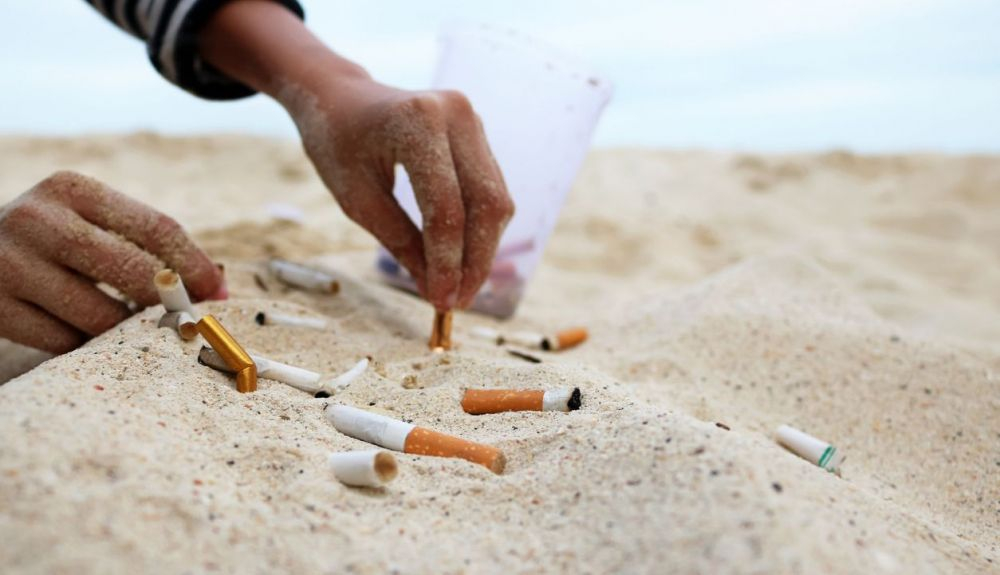 Una voluntaria recoge colillas y basura en la arena.
