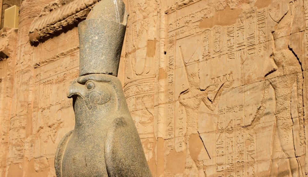 Estatua de Horus en el patio del Templo de Edfu con jeroglíficos en la pared, Edfu, Egipto Estatua de Horus en el patio del Templo de Edfu con jeroglíficos en la pared, Edfu, Egipto